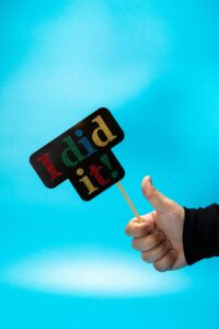 Close-up of a hand holding a colorful 'I did it!' sign against a blue background, symbolizing success.